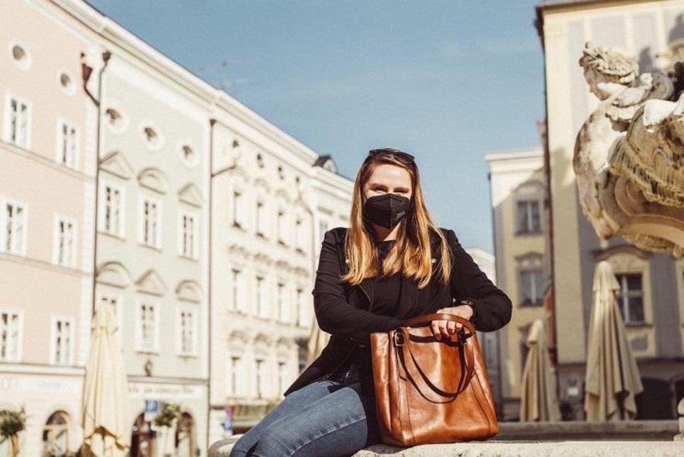 Kendall Taylor auf dem Residenzplatz in der Passauer Innenstadt, wie sie an einem Brunnen sitzt.